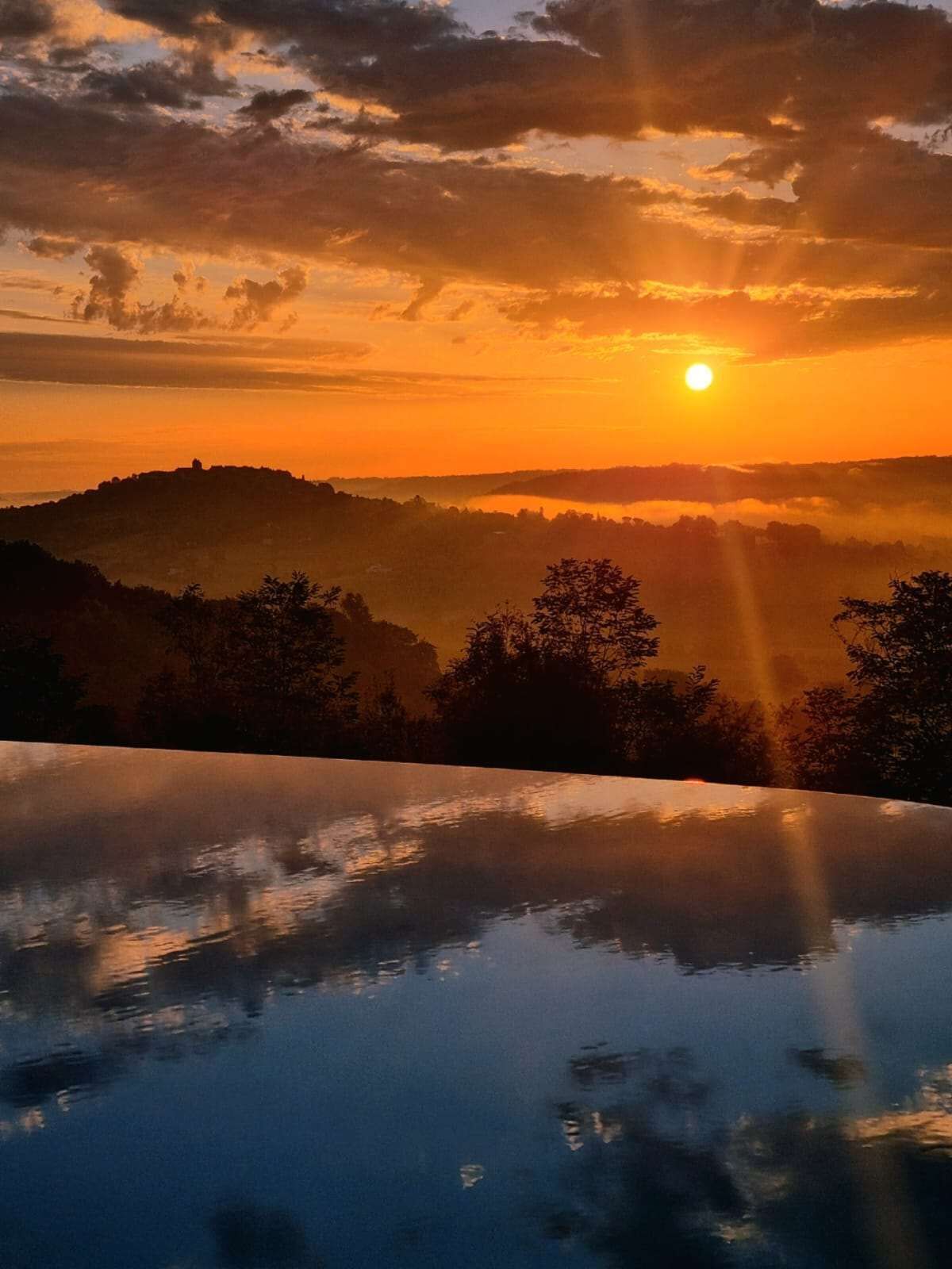 Een zonsondergang boven een glooiend landschap met een waterpartij die de lucht weerspiegelt.