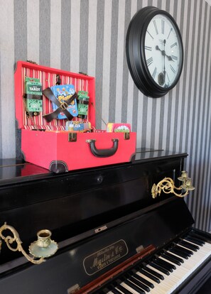 Une valise rouge contenant des jeux et une horloge posée sur un piano.