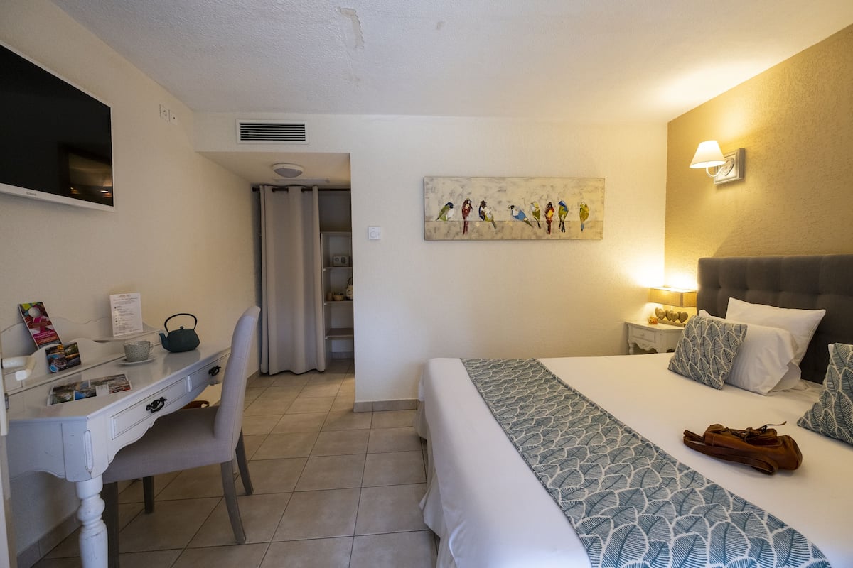 Een hotelkamer met een bed, bureau, stoel, televisie, schilderij en nachtkastje met lamp.
