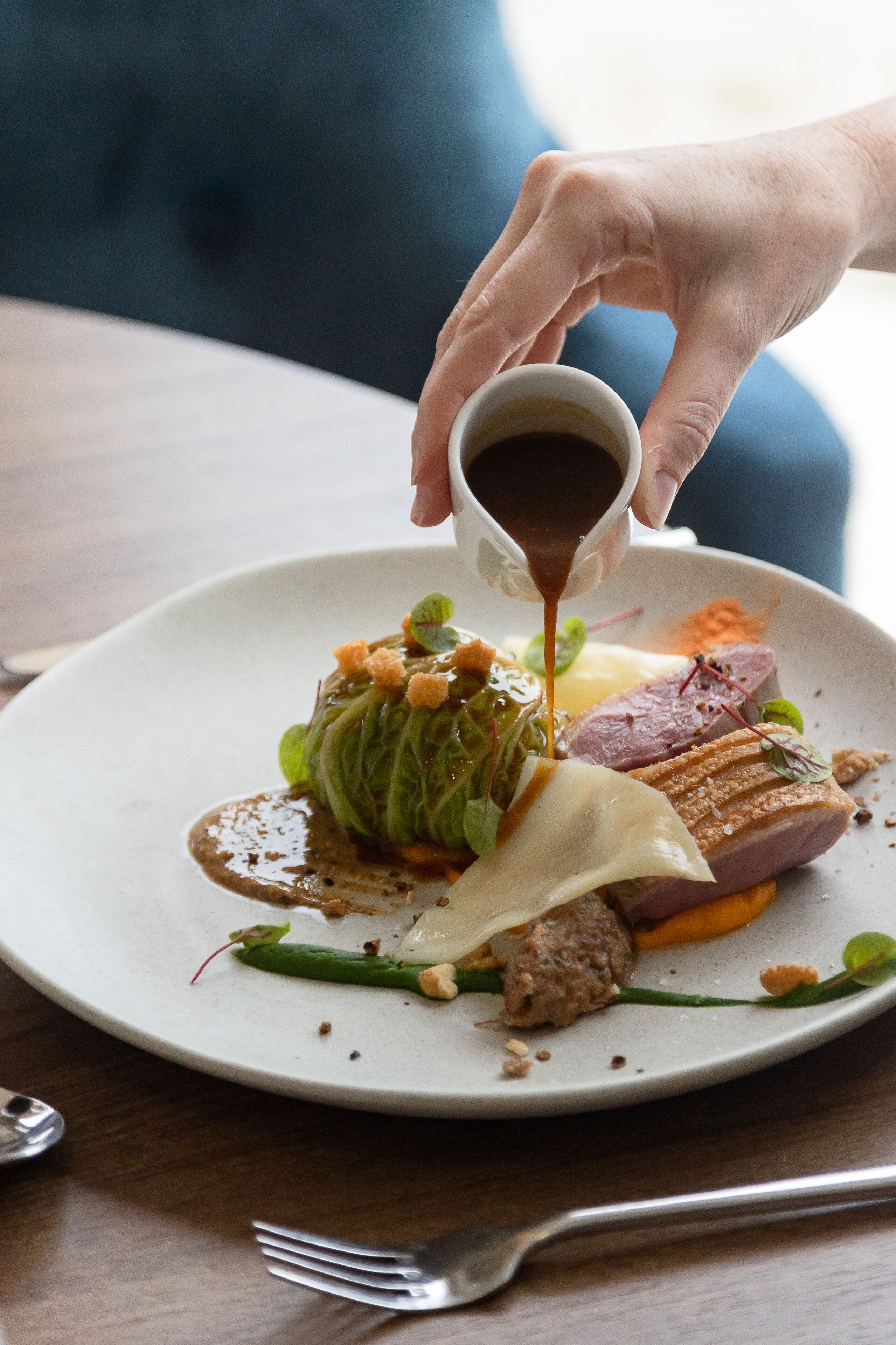 A person pouring sauce onto a plate of food.
