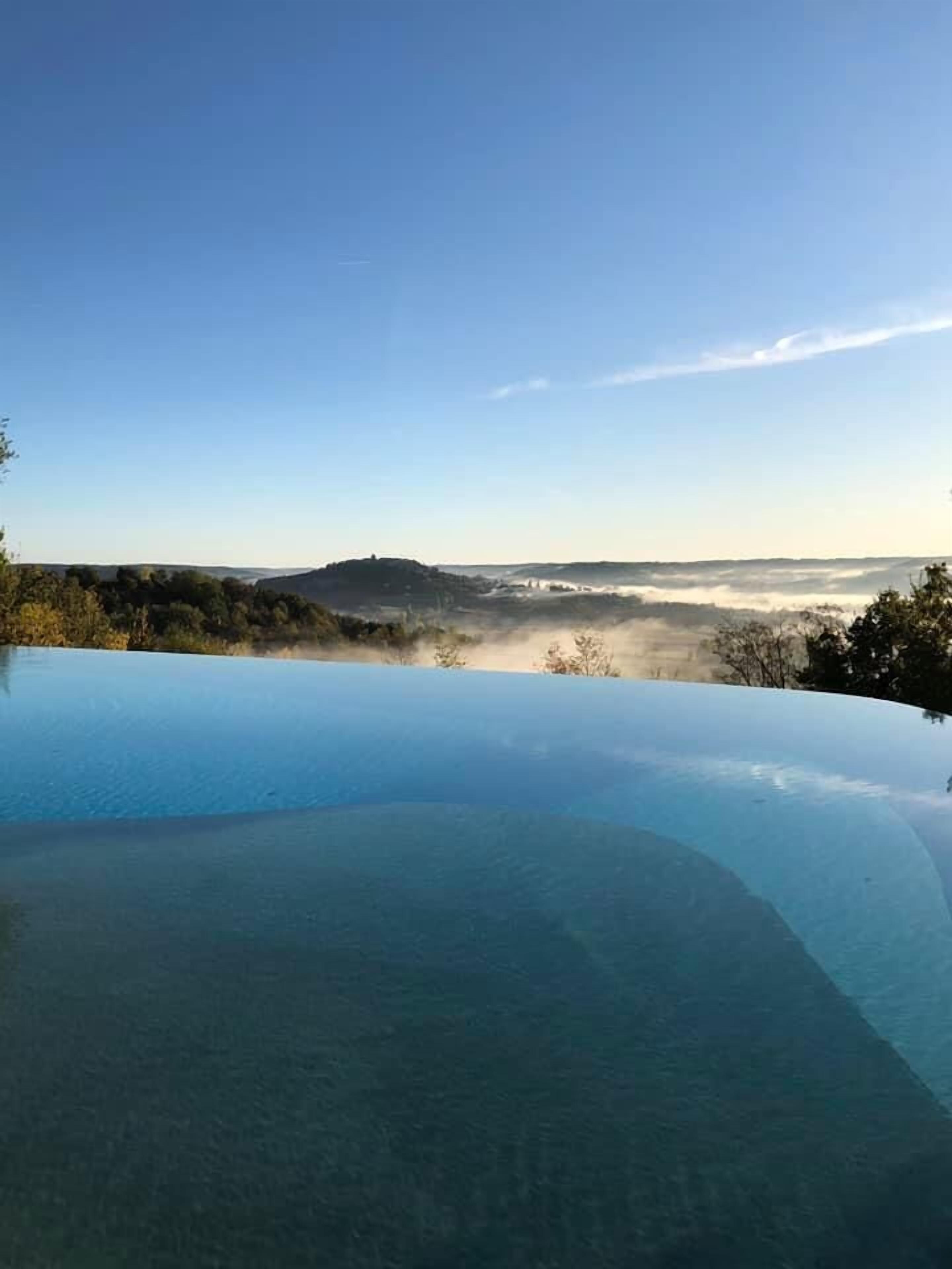 Une magnifique piscine à débordement d’un bleu profond, offrant une vue sur un paysage vallonné et une colline lointaine.