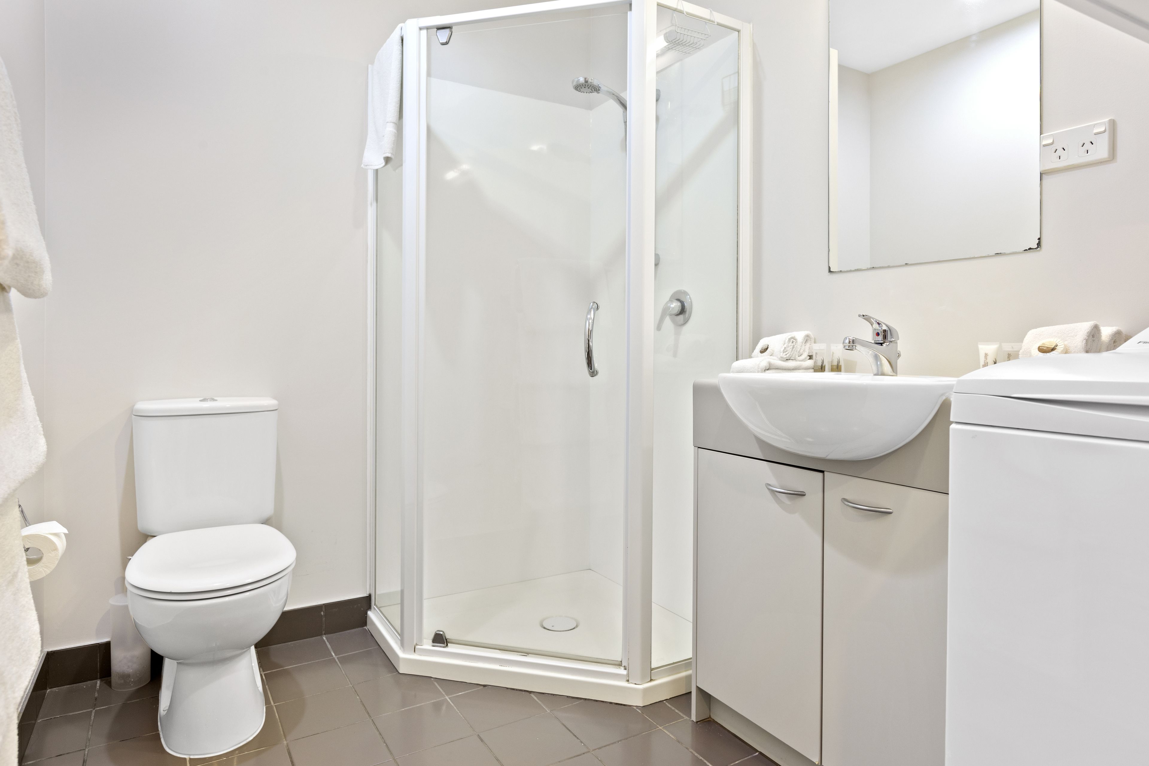 Un baño moderno con ducha envuelta en vidrio, inodoro blanco y tocador con lavamanos y espejo.