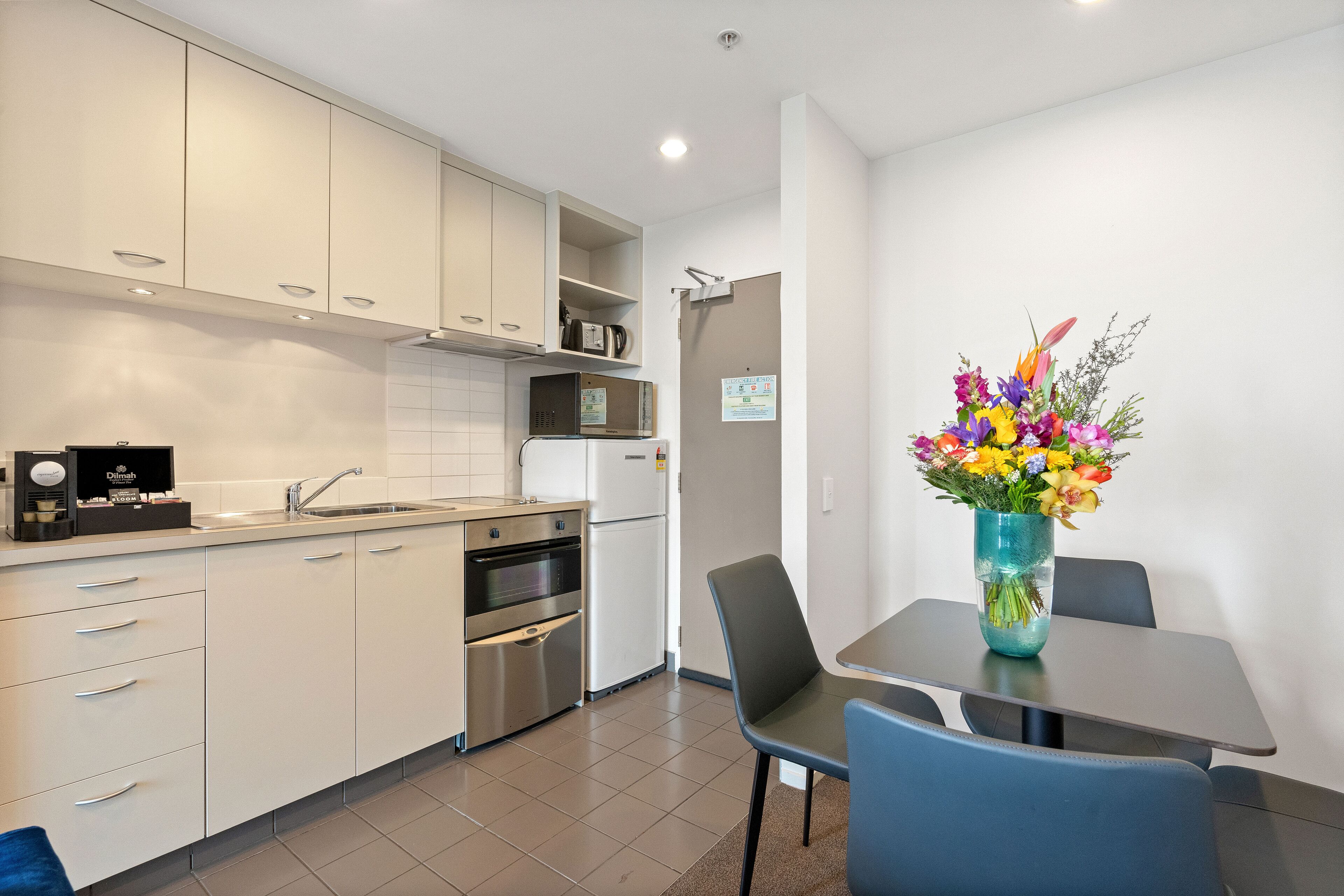 Une cuisine moderne avec des meubles blancs, un évier et un four à micro-ondes. On y trouve une table à manger avec des chaises et un vase de fleurs.