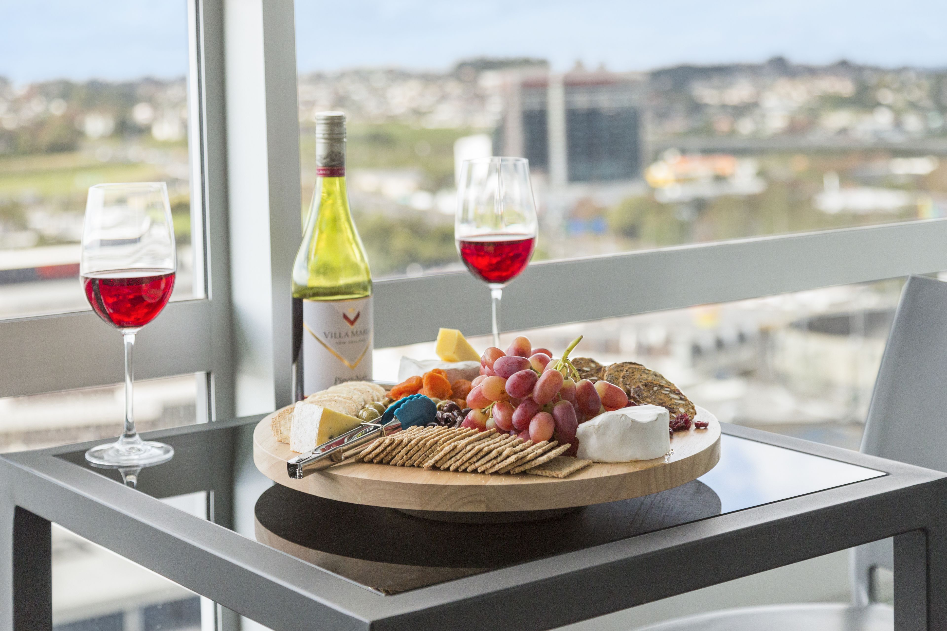 Une table avec une planche de fromages, des raisins, des crackers et des verres à vin.
