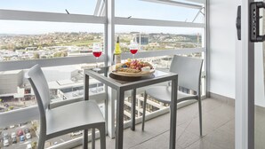 Un balcon avec une table dressée pour deux personnes, agrémentée d’un plateau de fruits et de verres à vin.
