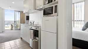 Une cuisine moderne avec des appareils électroménagers blancs, un coin repas offrant une vue agréable et une chambre dotée d’un lit et de rideaux.