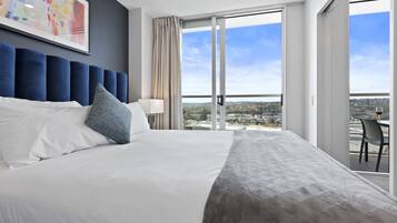 A hotel room with a large bed, a view of the city through floor-to-ceiling windows, and a painting on the wall.
