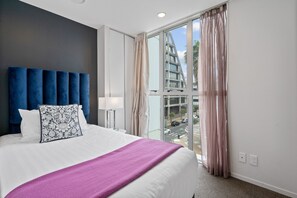 Een hotelkamer met een groot bed, een modern hoofdbord, uitzicht op de stad door grote ramen en een balkon met uitzicht op de straat.