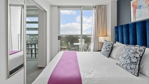 Une chambre d’hôtel avec un lit, un balcon doté d’une table et de chaises, et une vue sur le ciel.