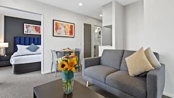 A modern hotel room with a bed, a sofa, a coffee table with a vase of flowers, and a desk with a chair.
