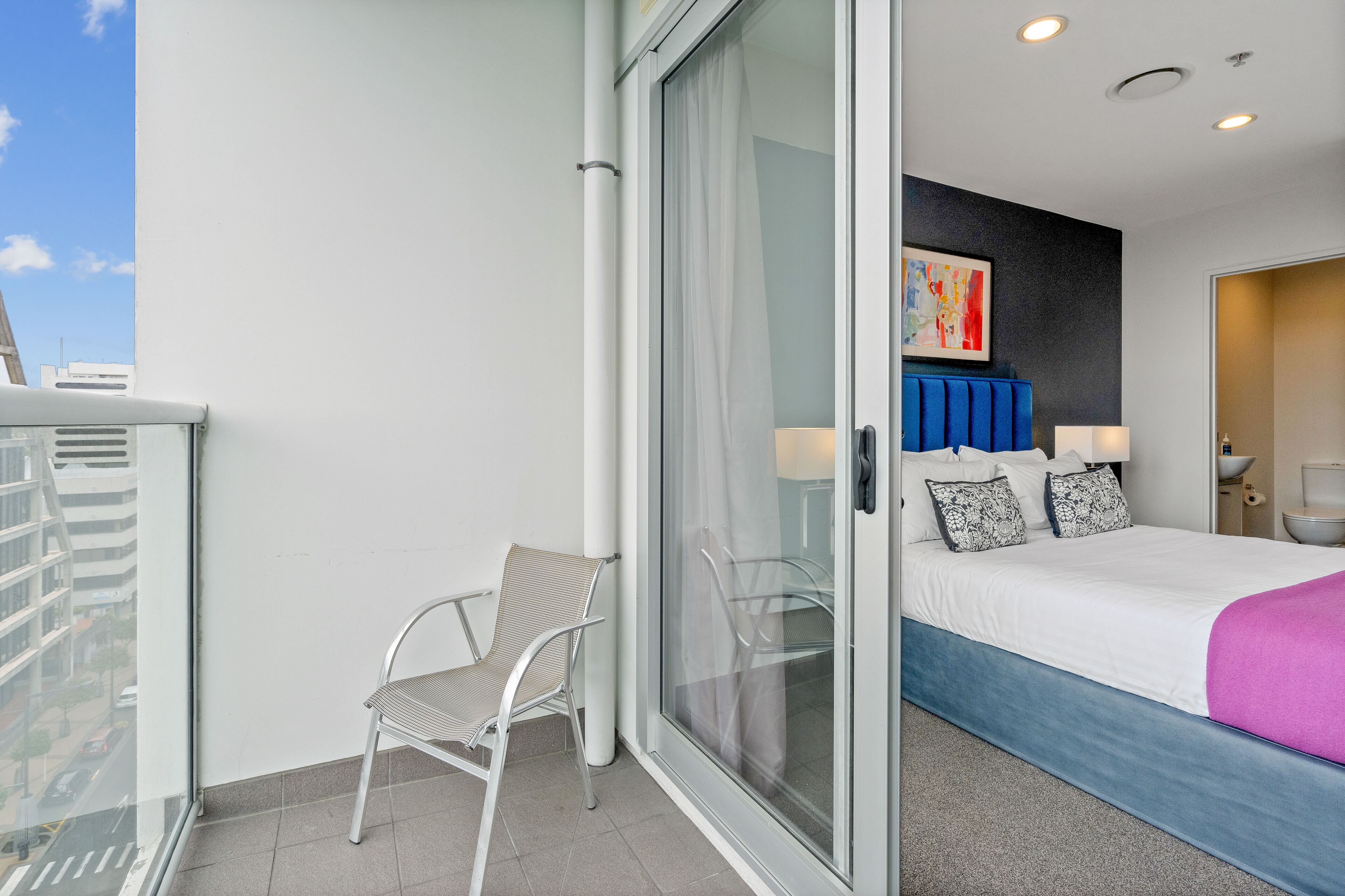Habitación de hotel con cama, una silla, puerta de vidrio y vista a la ciudad.