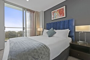 Een moderne hotelkamer met een groot bed, een nachtkastje, een raam met gordijnen en een schilderij aan de muur.