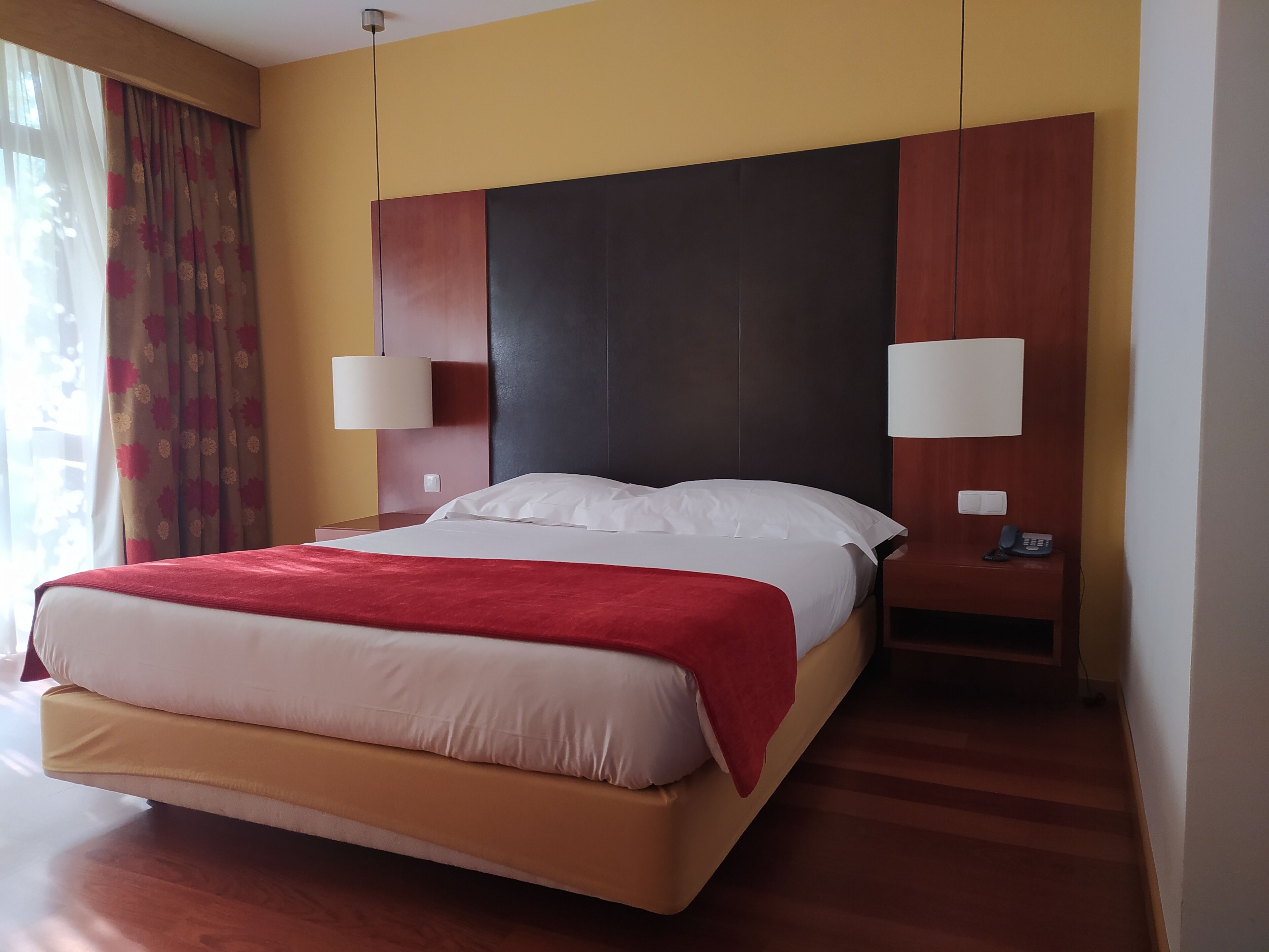 A hotel room with a large bed, two bedside lamps, a telephone, and a nightstand.