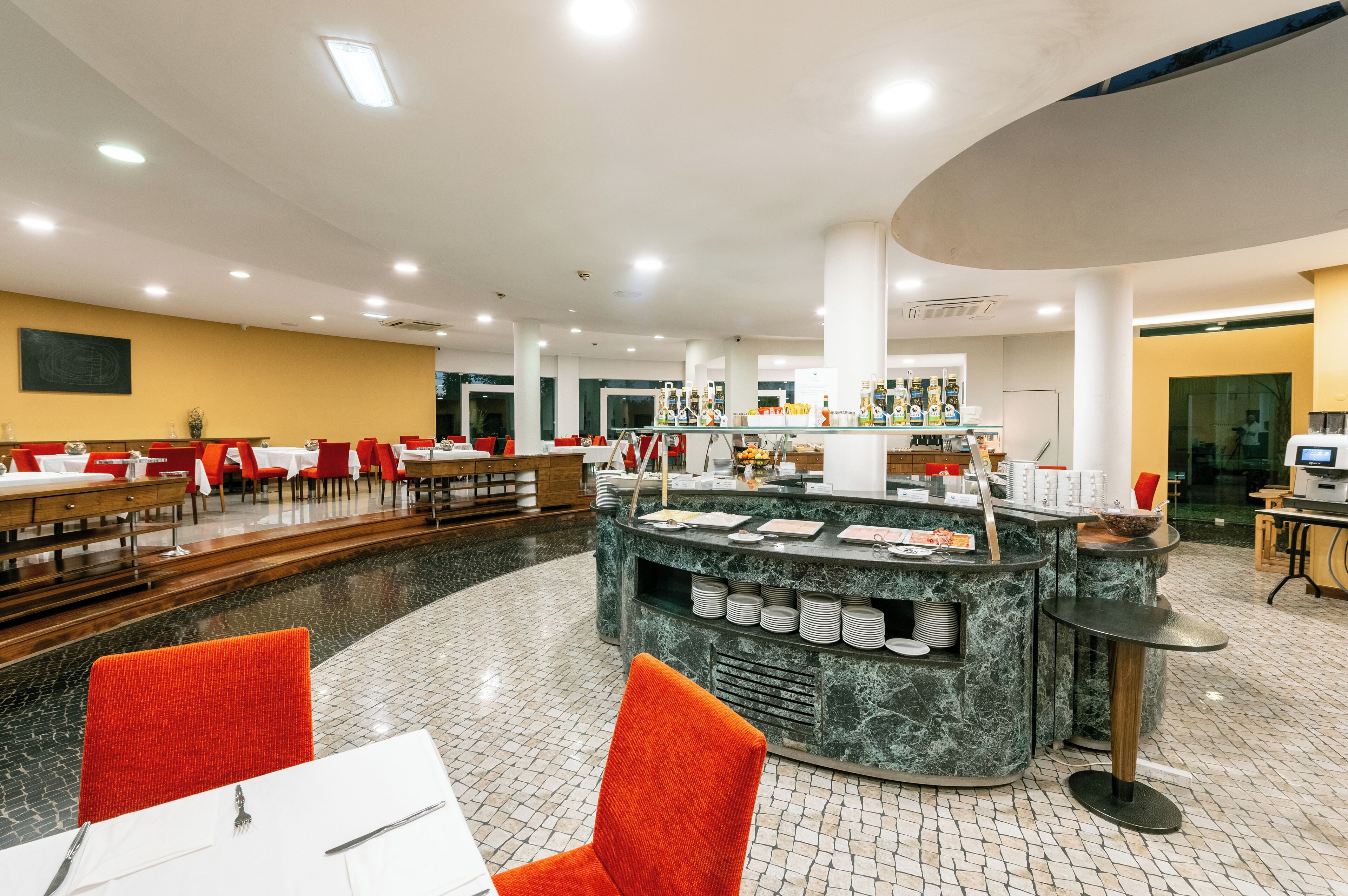 Un restaurante espacioso con techos altos, una zona de bar central y diversas opciones de asientos, incluyendo mesas y sillas.