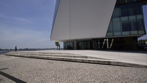 Un edificio moderno con fachada de vidrio y un área pavimentada en su parte frontal.