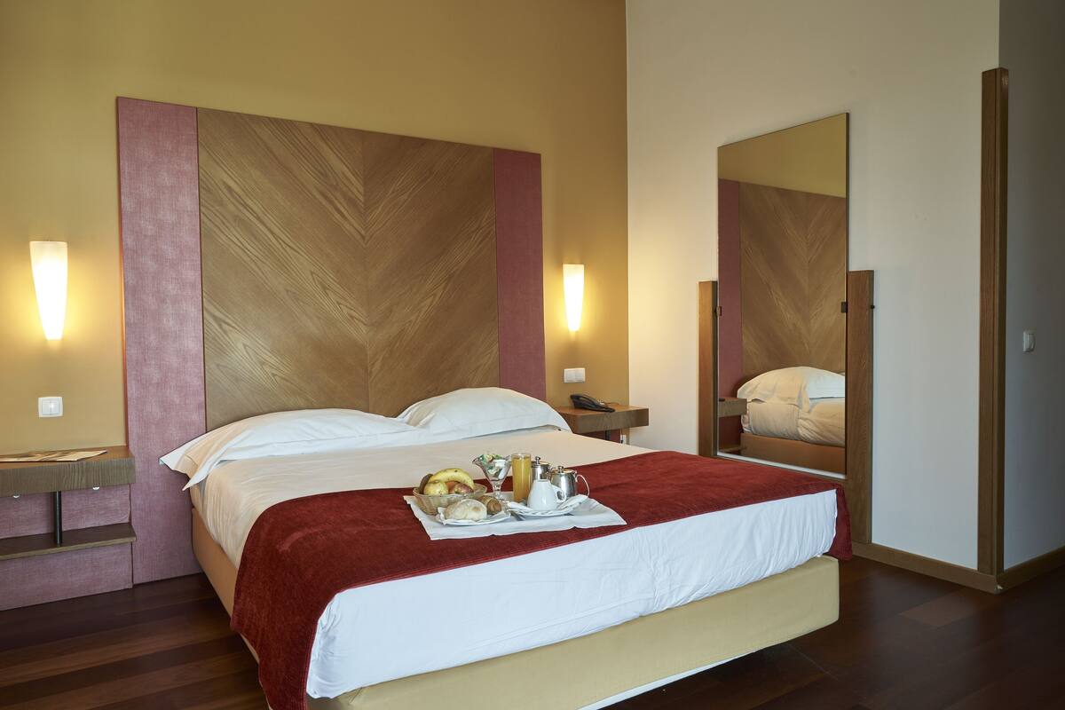 Ein Hotelzimmer mit einem großen Bett, einem Nachttisch, einem Spiegel und einer Wandleuchte.
