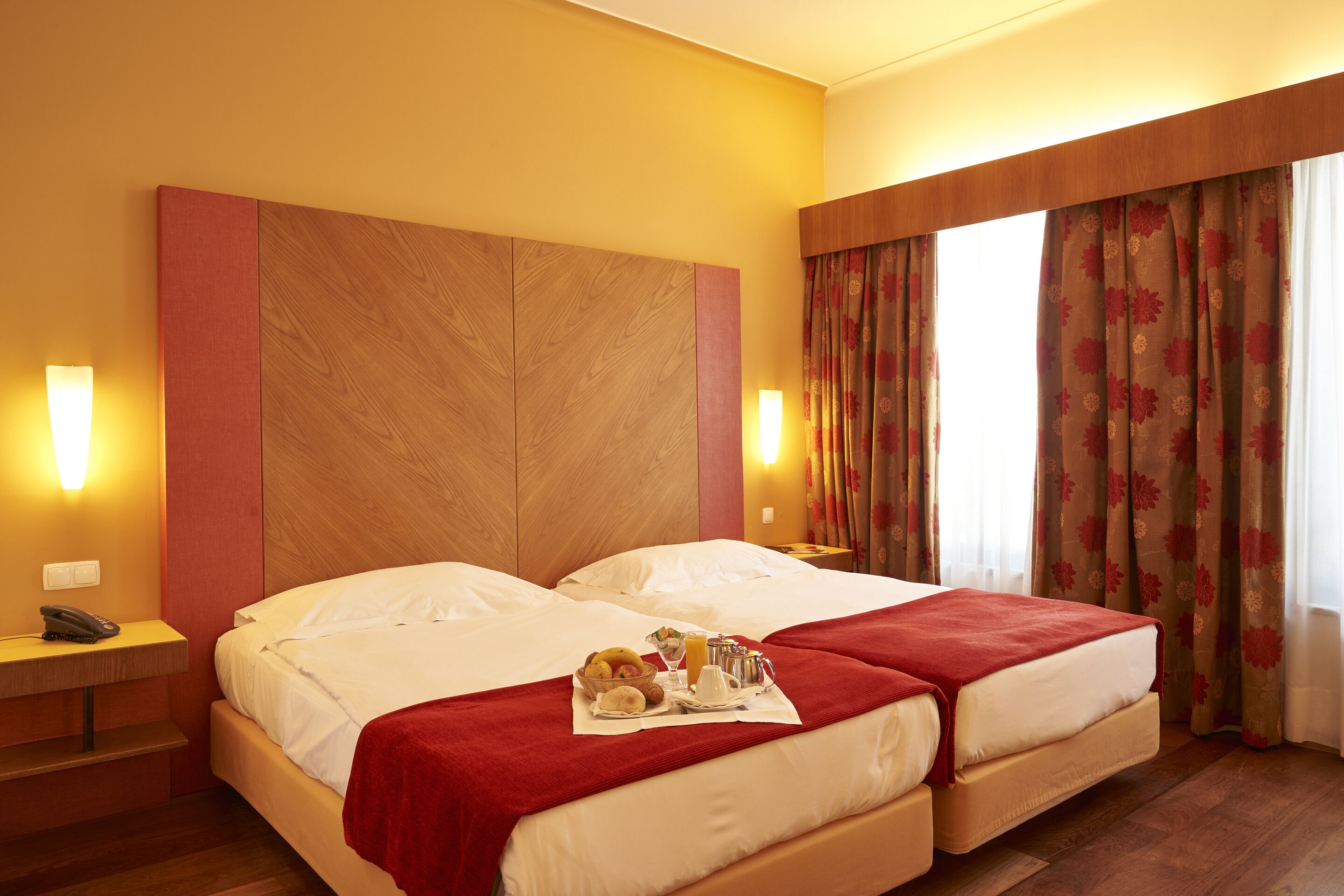 Habitación de hotel con dos camas, cabecera de madera, teléfono y bandeja de desayuno sobre las camas.