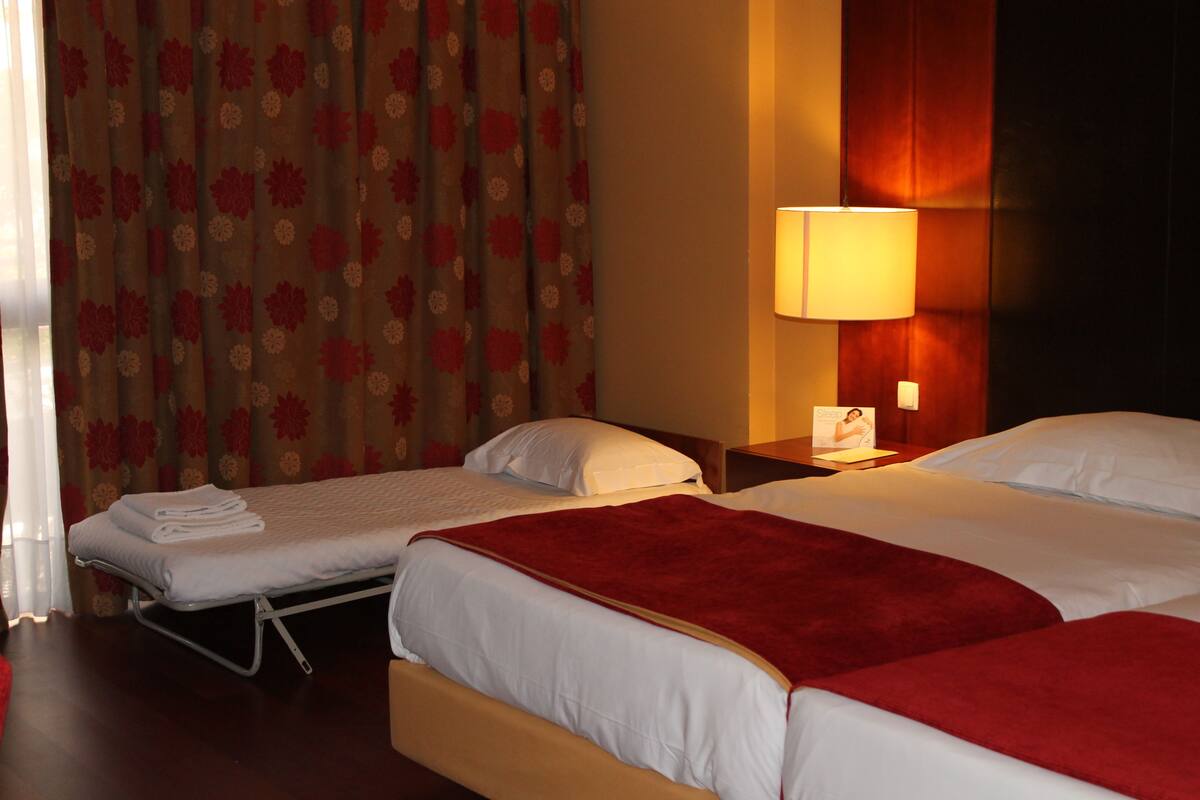 Ein Hotelzimmer mit zwei Betten, einem Nachttisch mit Lampe und einem Fenster mit Vorhängen.