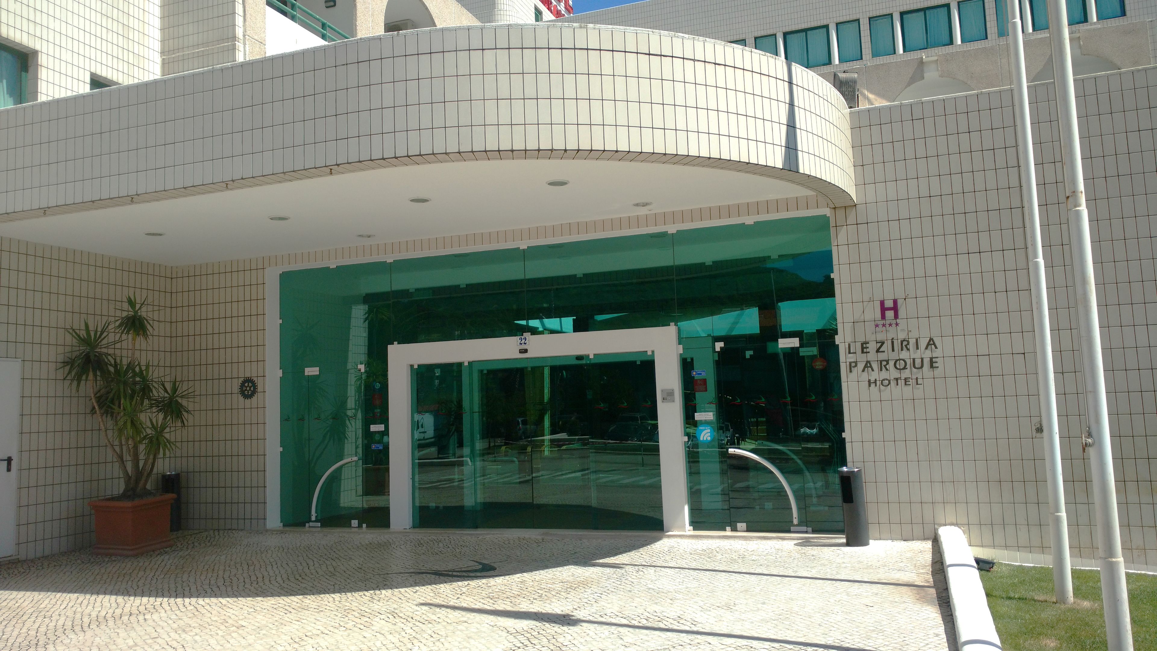 L’entrée d’un hôtel, avec une façade incurvée, des portes en verre et une enseigne indiquant « LEZIRI PARQUE HOTEL ».