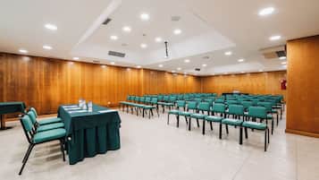 Une salle de conférence avec des rangées de chaises vertes, une table recouverte d’une nappe verte et des murs lambrissés.