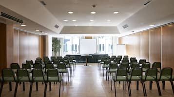 A conference room with rows of green chairs, a whiteboard, and a projector screen at the front.