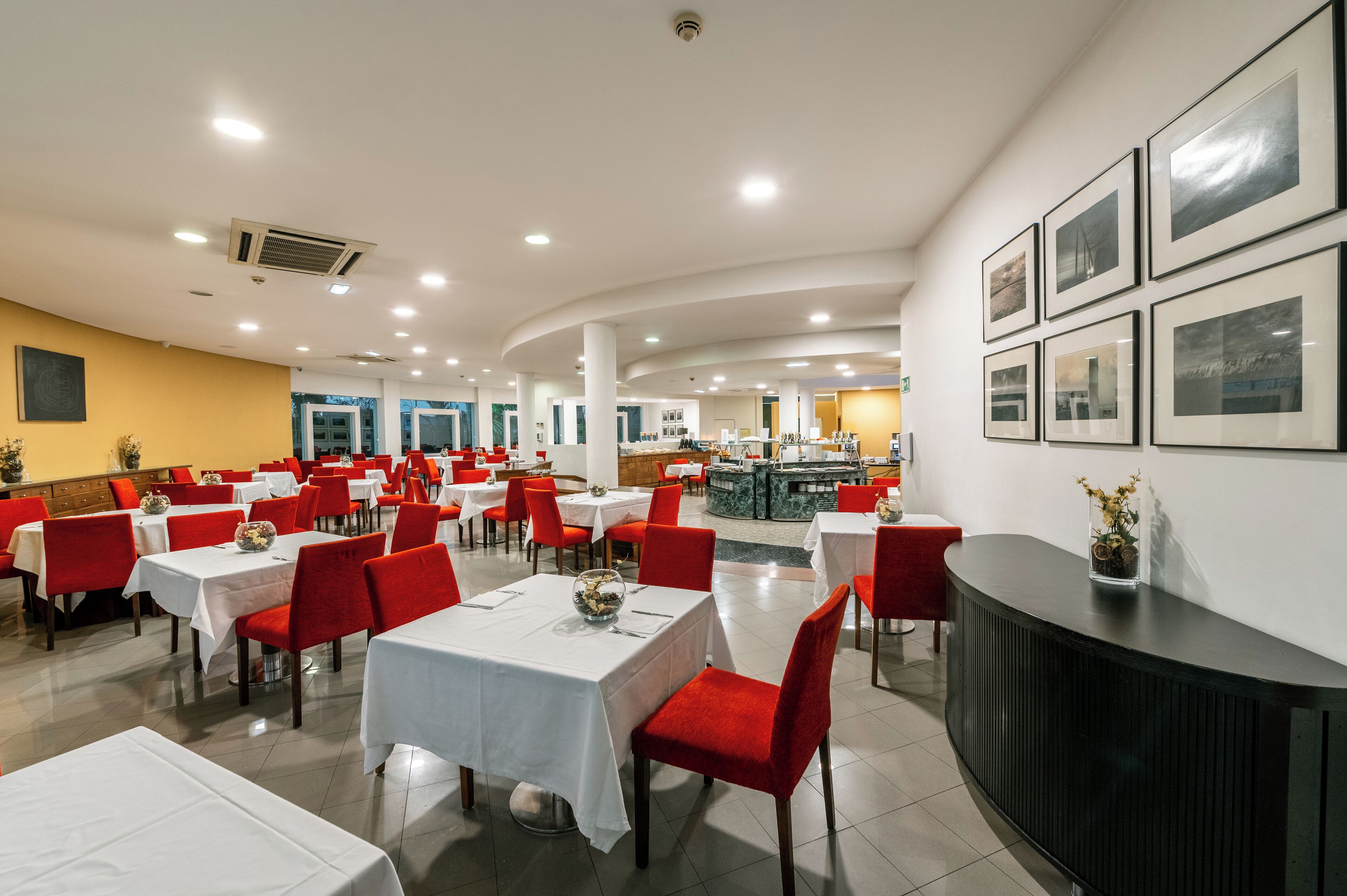 A spacious dining area with multiple tables and chairs, a reception desk, and framed pictures on the wall.