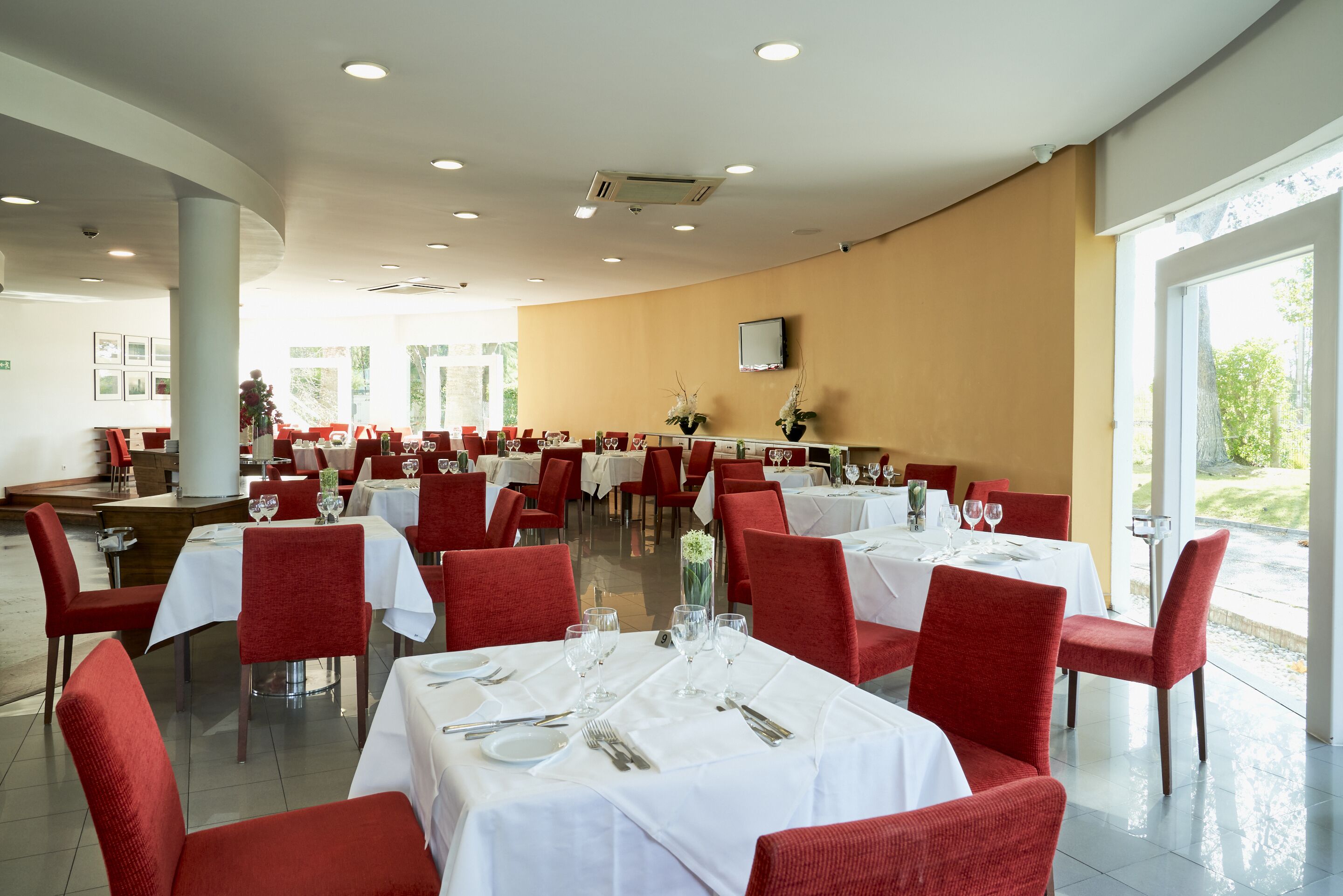 A spacious dining area with multiple tables and red chairs, featuring a modern interior design and large windows.