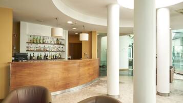A hotel lobby with a curved reception desk, a bar area with various bottles, and two leather chairs.