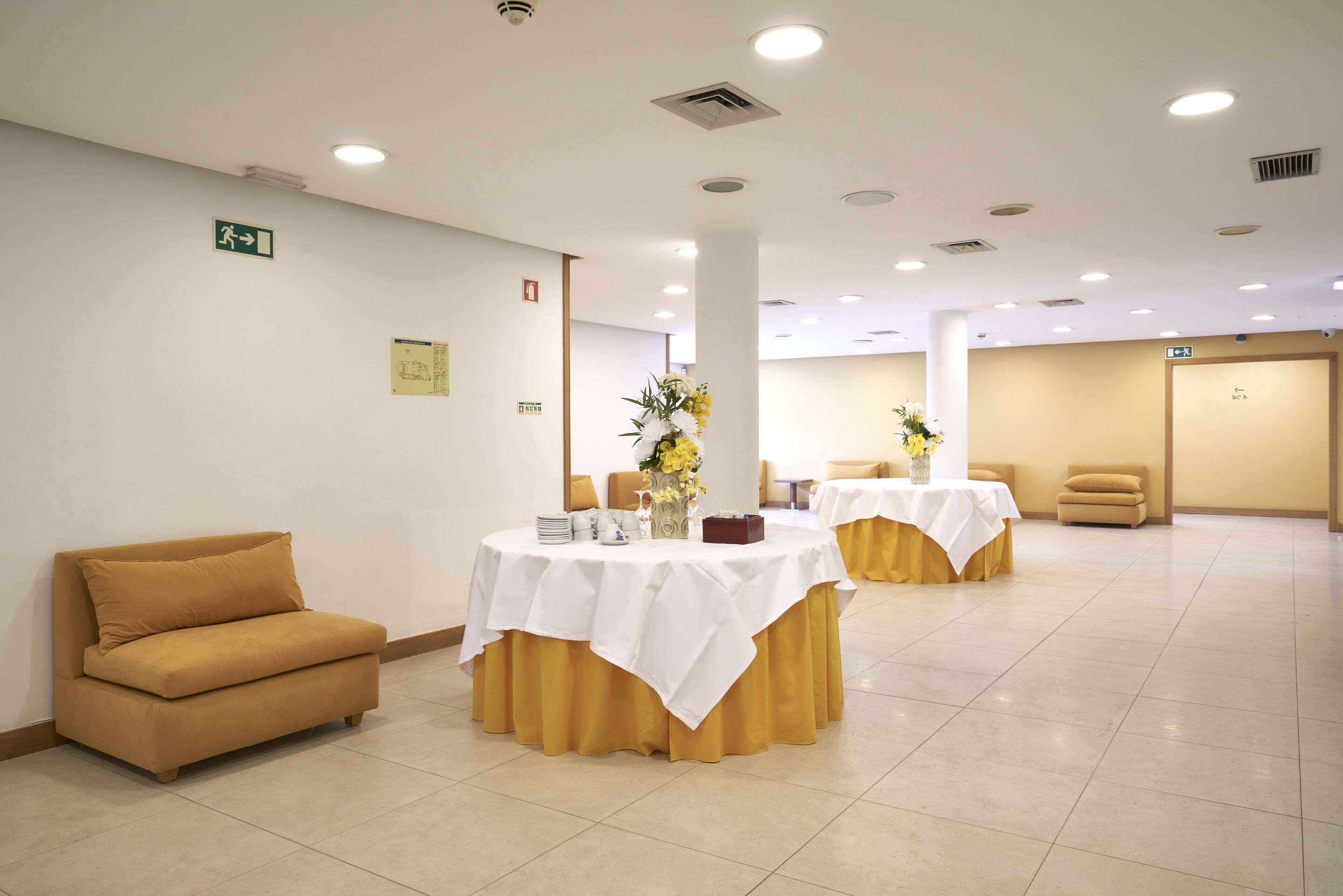 A hotel lobby with a sofa, two round tables with white tablecloths, and a vase of flowers.
