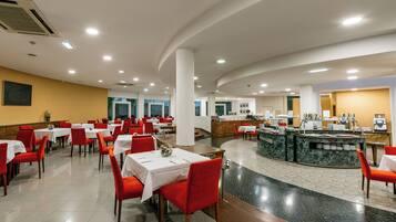 Un restaurante amplio con varias mesas y sillas rojas, una barra central con encimera de mármol y piso de baldosas.