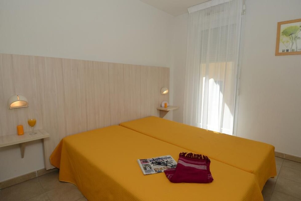 A hotel room with a bed, a nightstand, a lamp, a window with curtains, and a framed picture on the wall.