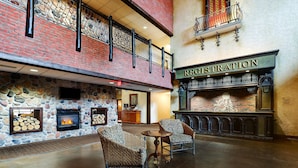 A lobby with a stone fireplace, wicker chairs, a registration desk, and a balcony with a railing. - Stoney Creek Hotel Sioux City (Sioux City)