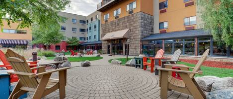 An outdoor patio area with Adirondack chairs, a circular brick pattern, and a building with multiple windows and balconies.