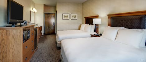 Habitación de hotel con dos camas, un televisor, un aparador de madera y una puerta que da a un pasillo.