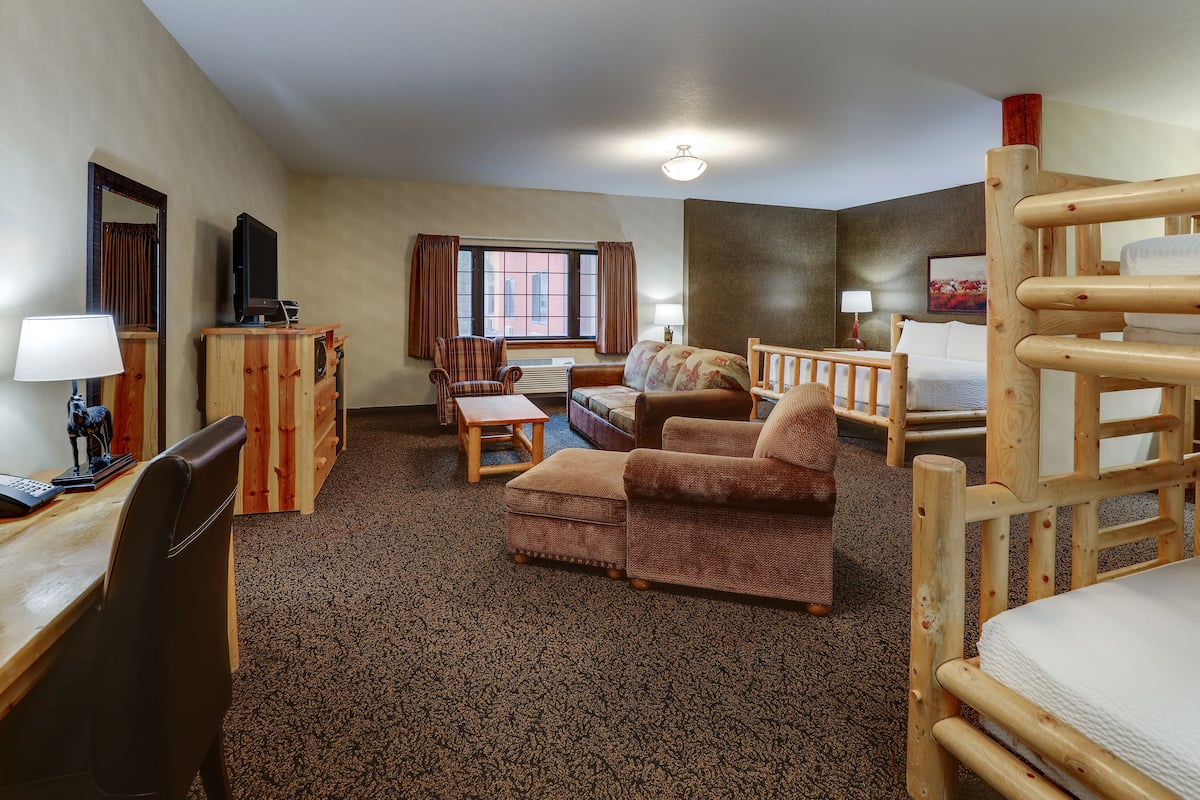 Une chambre d’hôtel avec un bureau en bois, un canapé, une chaise, un lit et une fenêtre avec des rideaux.