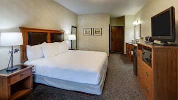 A hotel room with a large bed, wooden headboard, bedside tables with lamps, a dresser with a flat-screen TV, and framed pictures on the wall.