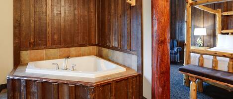 Un baño de estilo cabaña de madera con una bañera independiente, un banco de madera y un cabecero de madera.