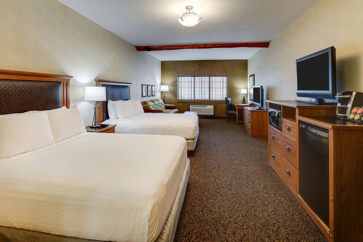 Une chambre d’hôtel avec deux lits, un bureau, une télévision, une machine à café et une commode.