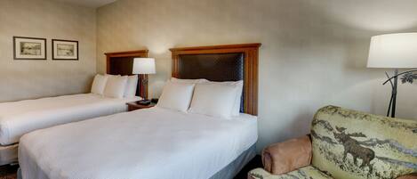 A hotel room with two single beds, a wooden headboard, a lamp, and a patterned armchair.