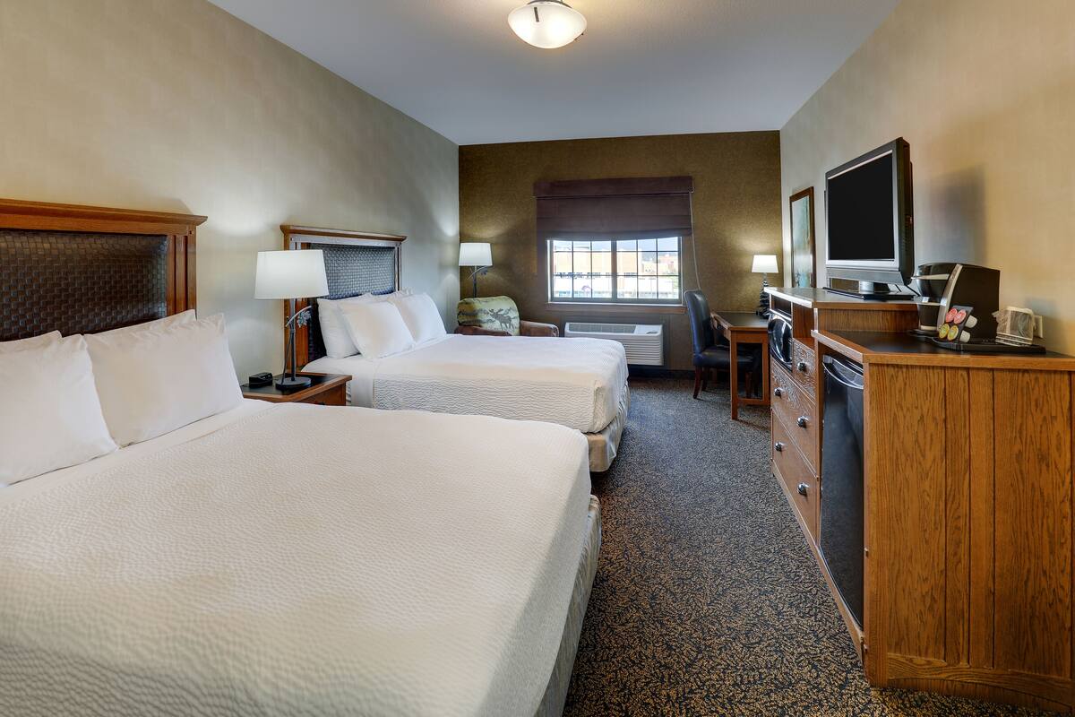 Une chambre d’hôtel avec deux lits, un bureau avec une télévision, une commode et une fenêtre avec des stores.