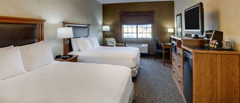 A hotel room with two beds, a desk with a television, a dresser, and a window with blinds.