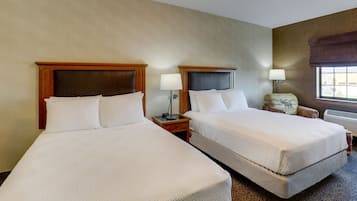 Habitación de hotel con dos camas, una mesita de noche con lámpara, una silla y ventana con vistas.