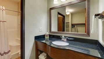 A bathroom with a large mirror, a sink, and a shower area.
