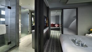 Una habitación de hotel moderna con cabina de ducha de vidrio, una cama con una bandeja de desayuno y vistas a otra habitación con una cama y una mesita de noche.