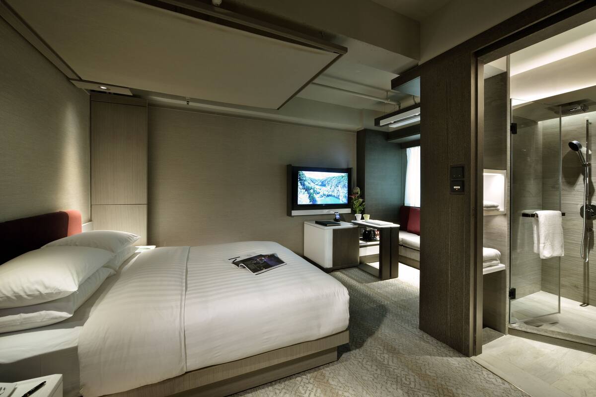 Une chambre d’hôtel moderne équipée d’un grand lit, d’un bureau, d’une télévision et d’un espace douche.