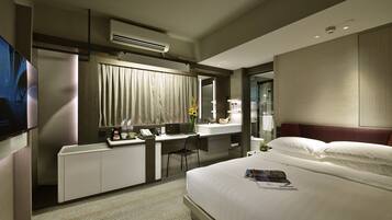 A modern hotel room with a bed, a desk, a chair, a TV, and a bathroom.