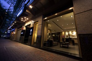A hotel entrance with a glass facade, a modern interior visible through the windows, and a brick-paved walkway outside. - Xi Hotel (Kowloon)