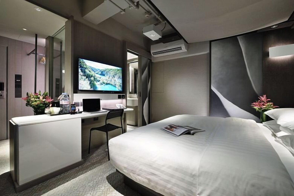 A modern hotel room with a bed, desk, and television.