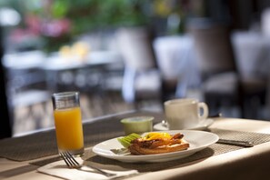 A breakfast setting with a plate of food, a glass of orange juice, and a cup on a table with a placemat. - Xi Hotel (Kowloon)