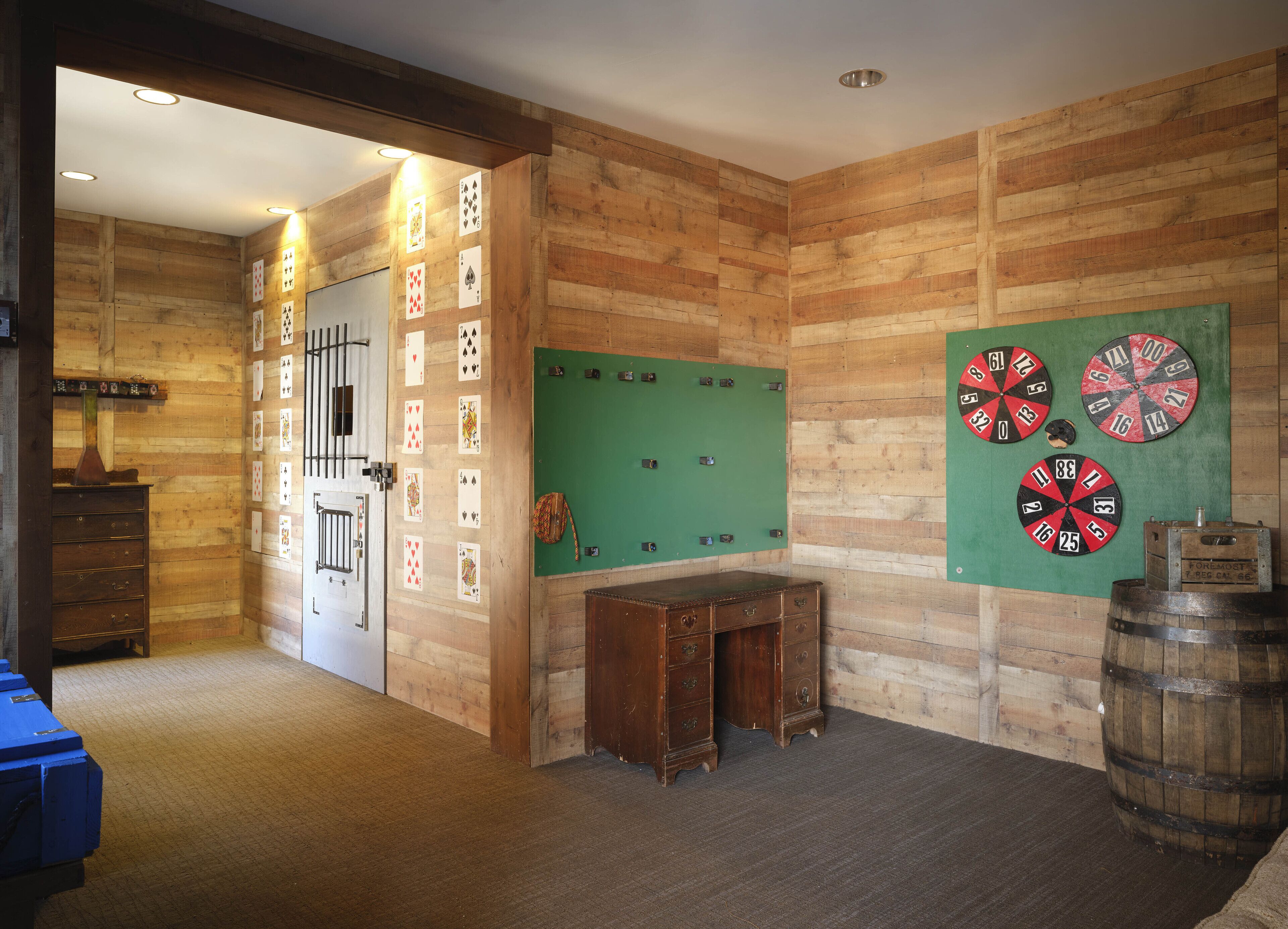 A room with wooden walls, a green pool table, four dartboards, and a wooden chest of drawers.